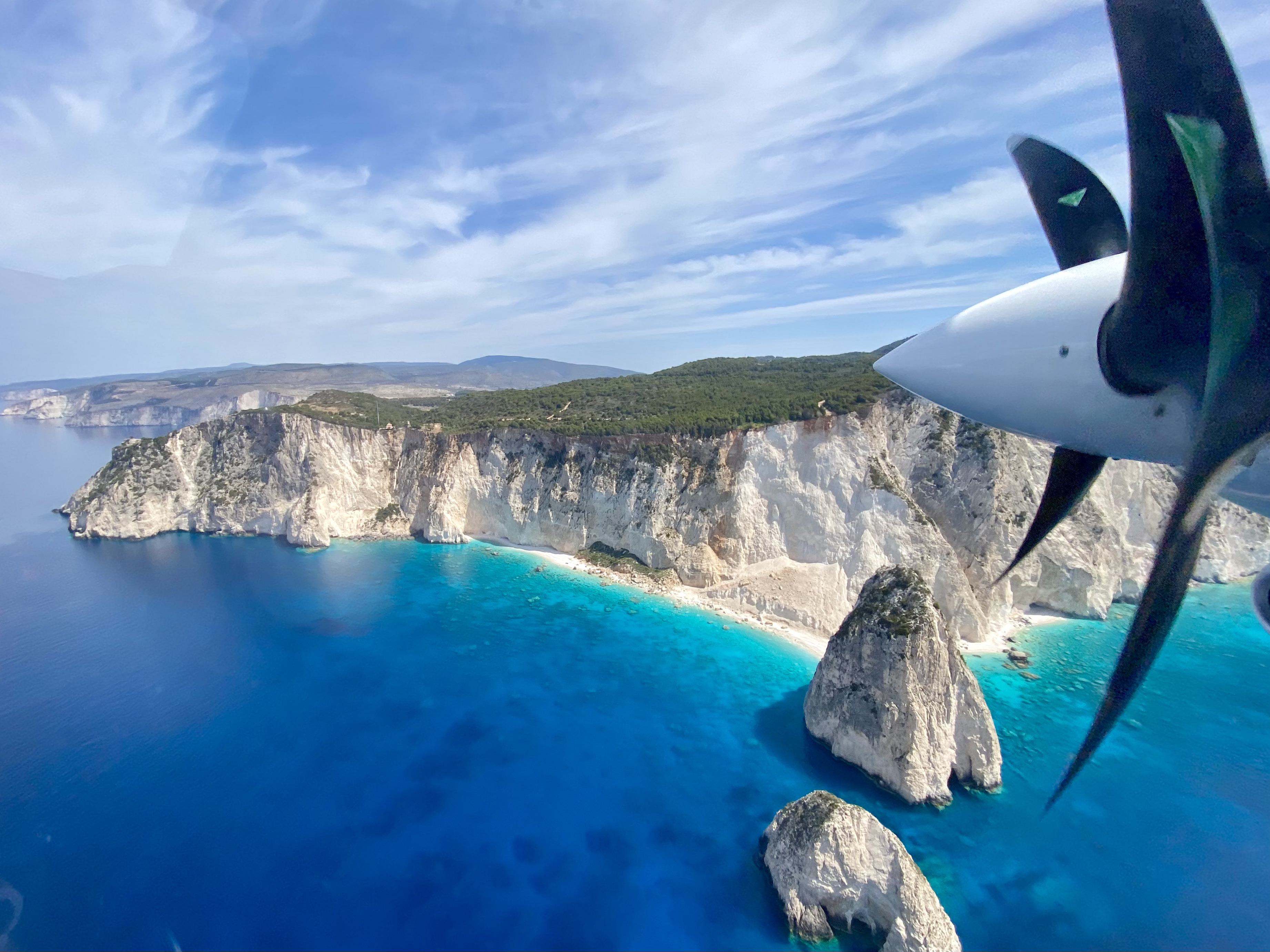Ionian coast seen from the cockpit of a Britten Norman Islander with a spinning propeller at the right edge of the frame