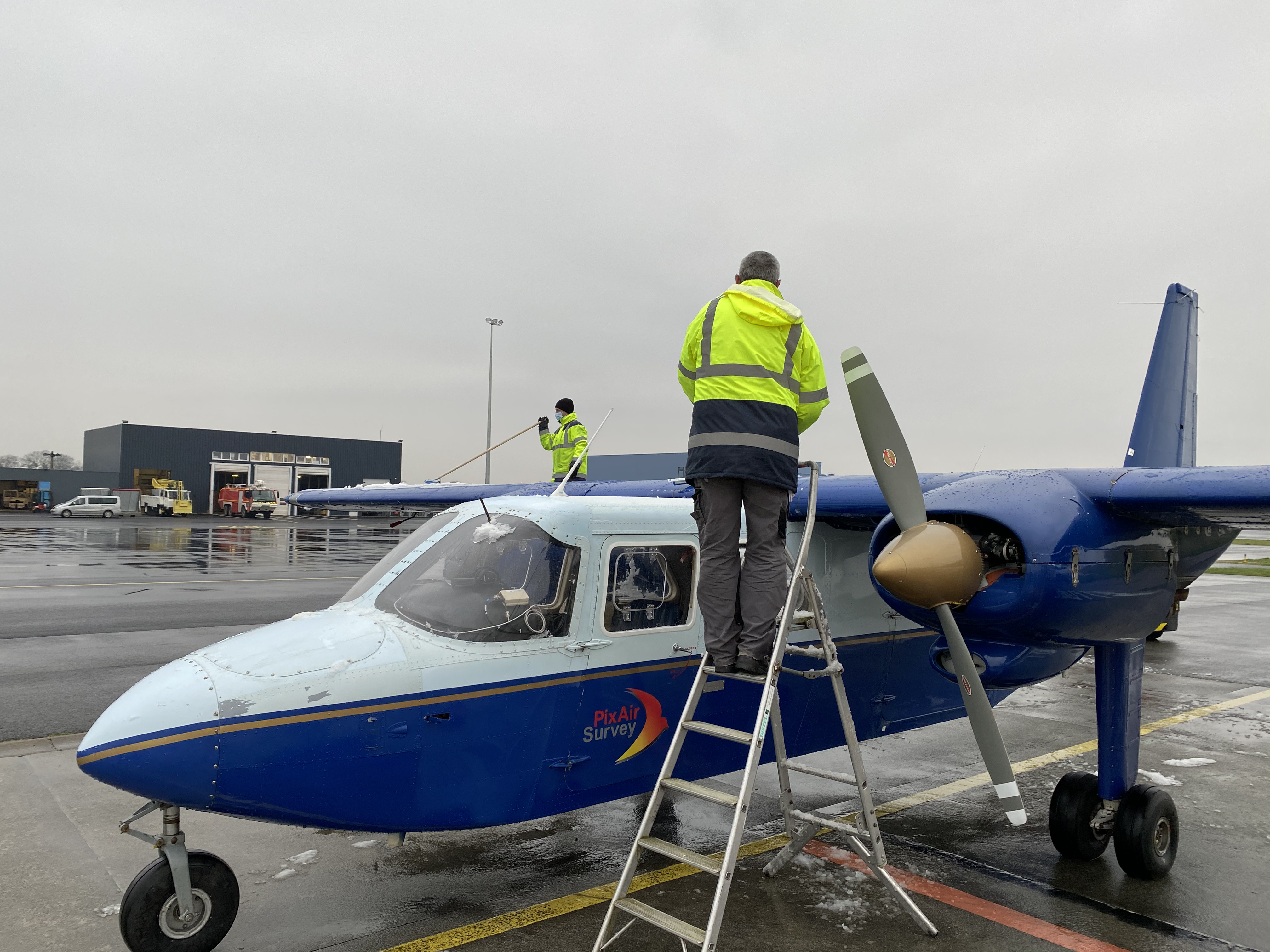 Two men in high visibility jackets scraping ice off F-HSUR in Caen