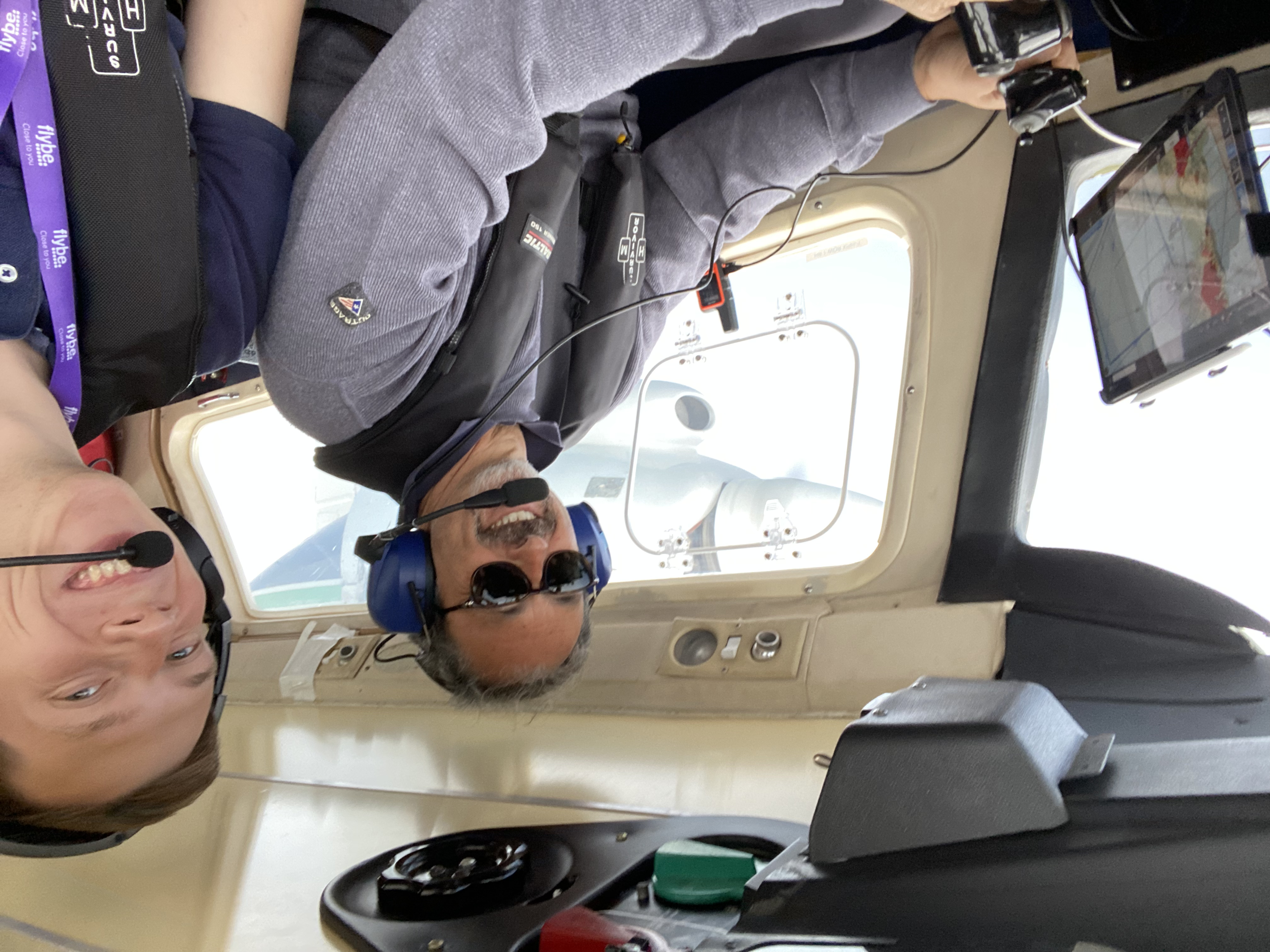 Two men smiling at the camera from the cockpit of a BN-2, one of them with his hands on the controls