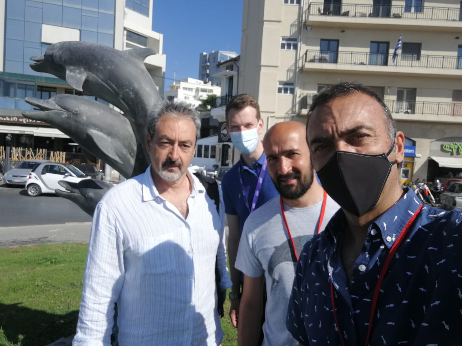 Four men posing in front of a statue of dolphins in a busy roundabout