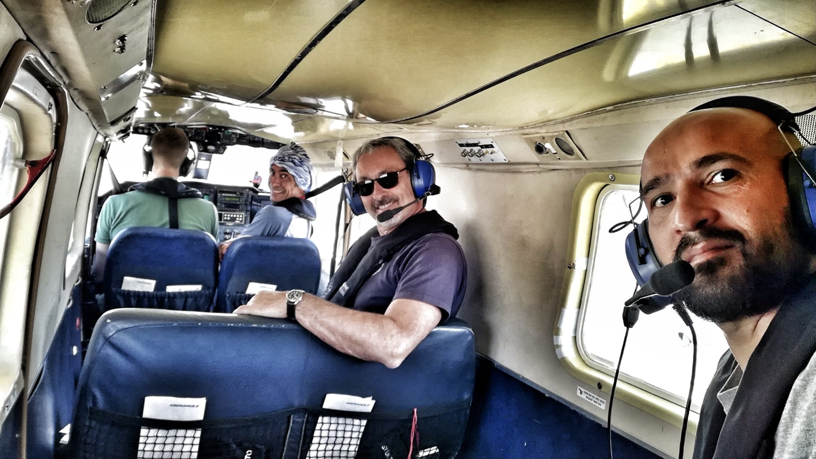 A man taking a selfie from the rear of a BN-2 showing two other men smiling and the pilot with his back turned to the camera