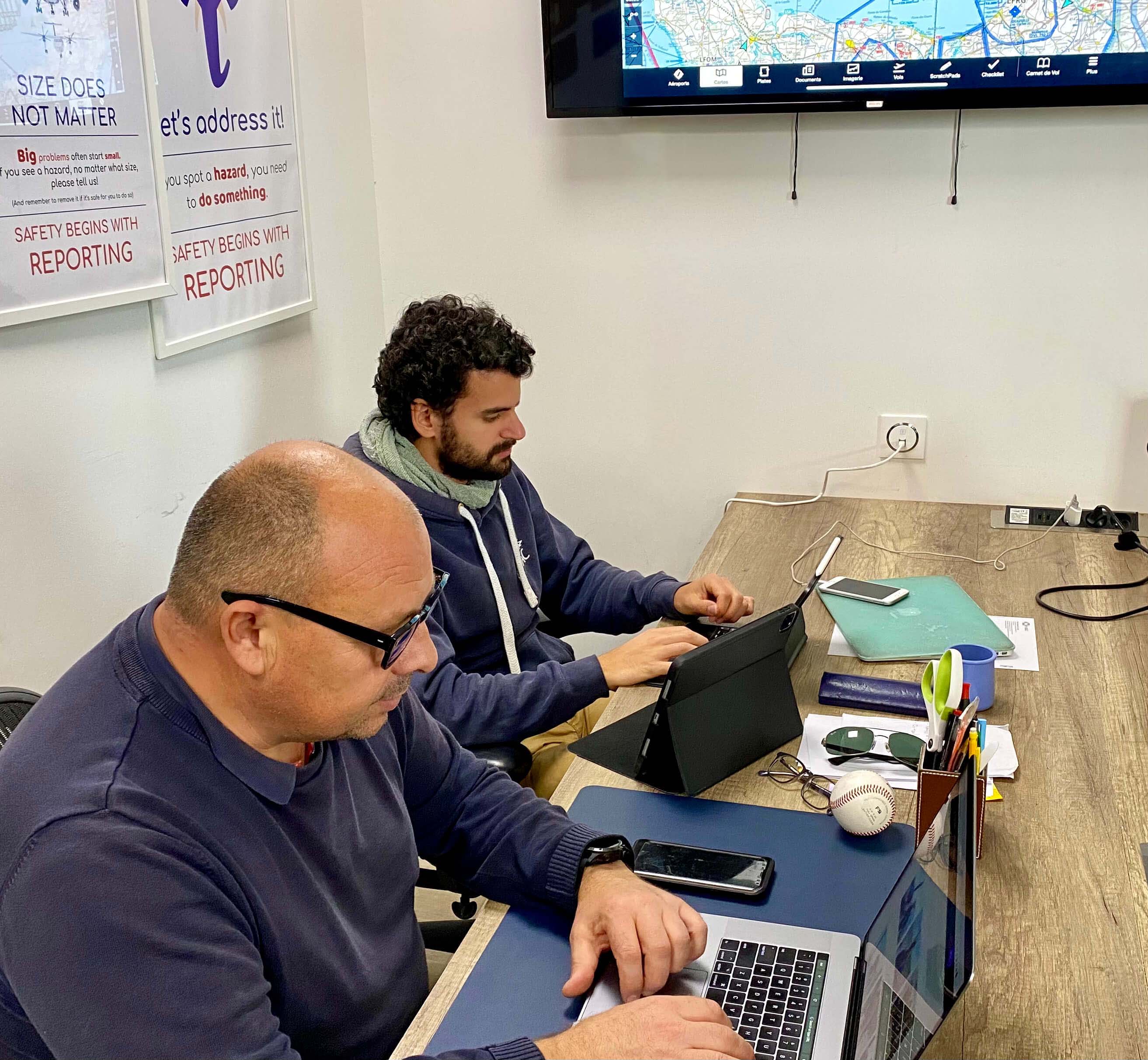 Two men working sitting at a table working on their computers