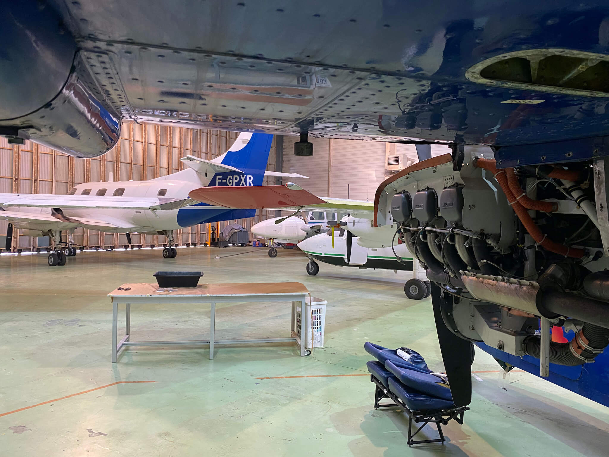 Aircraft in hangar seen from underneath an airplane wing with a uncowled piston engine